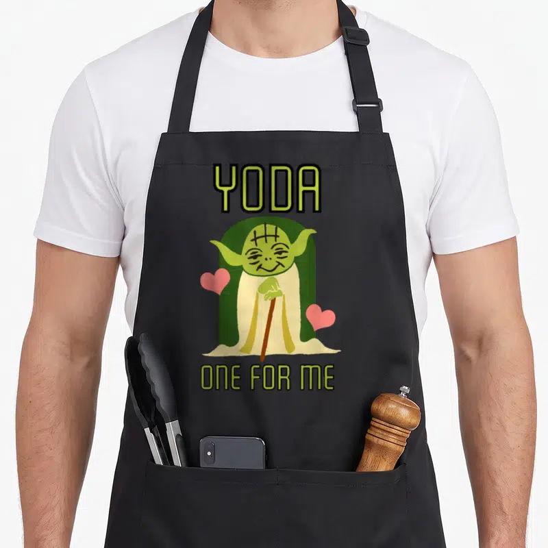 Yoda valentine's day apron - Cartoon Yoda holding a cane between two pink hearts with text YODA and ONE FOR ME — shown on a black cotton canvas apron against a white background