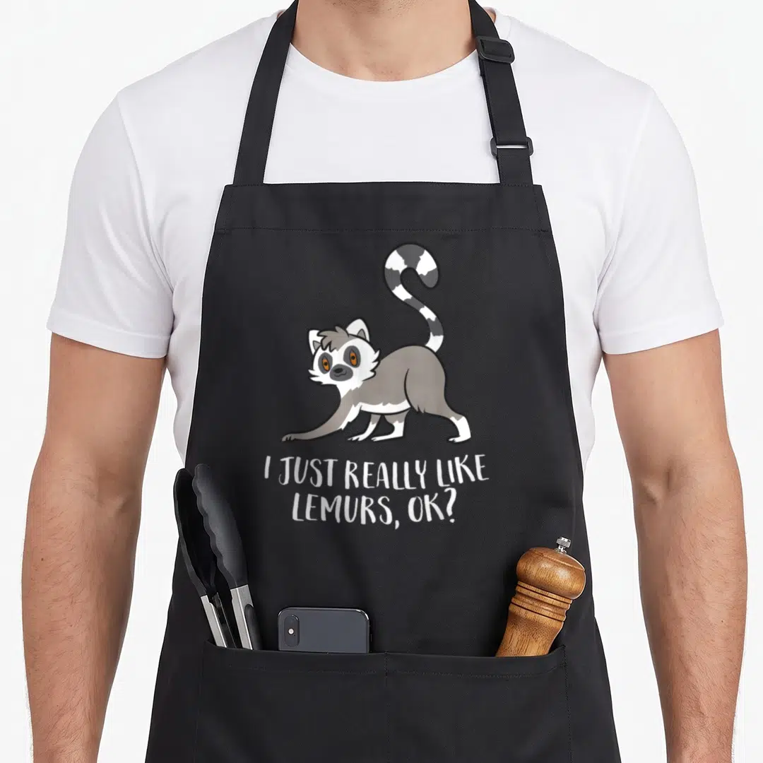 Lemur apron for men - Cartoon lemur stretching with white text I JUST REALLY LIKE LEMURS, OK? below — shown on a black cotton canvas apron against a white background
