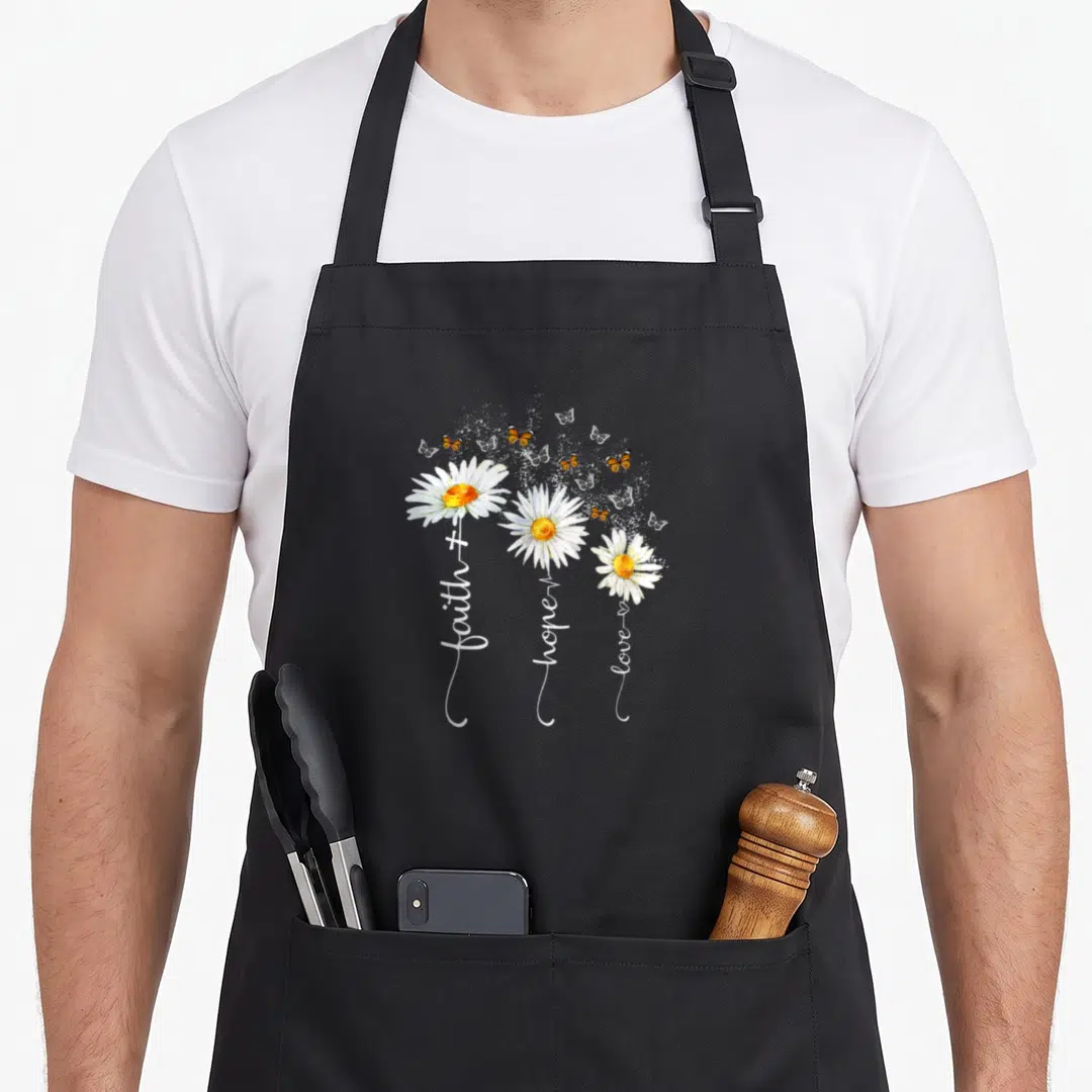 Faith butterfly apron - Three daisies with faith hope love text and orange butterflies — shown on a black cotton canvas apron against a white background