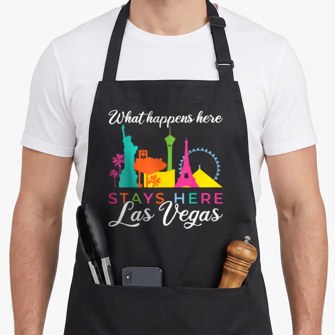 Stay vegas girls apron - Colorful Las Vegas skyline silhouettes with stacked text What happens here STAYS HERE Las Vegas — shown on a black cotton canvas apron against a white background
