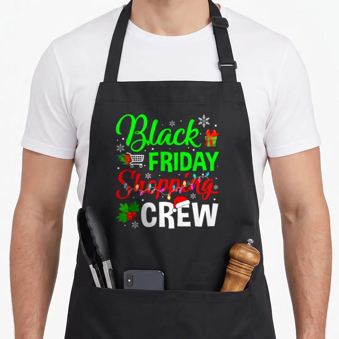 Crew christmas black friday apron - Stacked text reading Black FRIDAY Shopping CREW with Santa hat, cart, lights — shown on a black cotton canvas apron against a white background