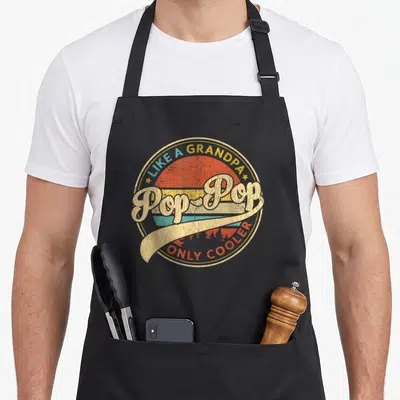 Cooler father day apron - Retro circular graphic with Pop-Pop text over yellow orange teal striped sunset background — shown on a black cotton canvas apron against a white background