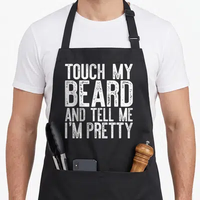 Cute touch beard apron - White stacked text reading TOUCH MY BEARD AND TELL ME I'M PRETTY — shown on a black cotton canvas apron against a white background