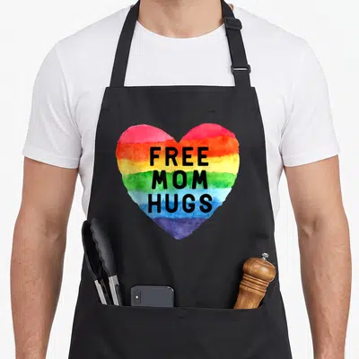 Hug gay pride apron - Rainbow watercolor heart with stacked black text reading FREE MOM HUGS — shown on a black cotton canvas apron against a white background