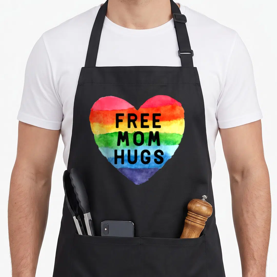 Hug gay pride apron - Rainbow watercolor heart with stacked black text reading FREE MOM HUGS — shown on a black cotton canvas apron against a white background