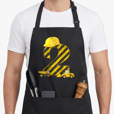 Digger 2nd apron - Yellow number 2 with hazard stripes, hard hat, dump truck and bulldozer — shown on a black cotton canvas apron against a white background