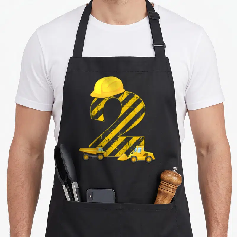 Digger 2nd apron - Yellow number 2 with hazard stripes, hard hat, dump truck and bulldozer — shown on a black cotton canvas apron against a white background
