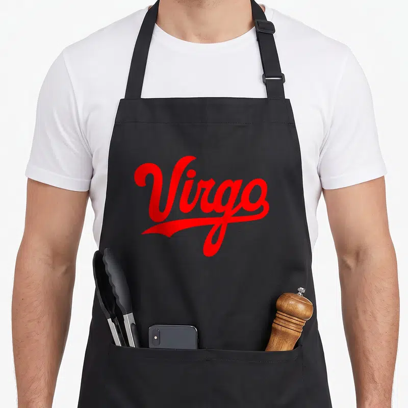 Season zodiac aprons - Red cursive Virgo text with underline flourish on grey background — shown on a black cotton canvas apron against a white background