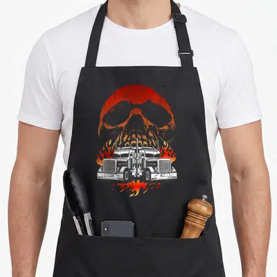 Trailer truckin semi truck apron - Two white semi-trucks facing forward surrounded by orange flames with a large orange — shown on a black cotton canvas apron against a white background