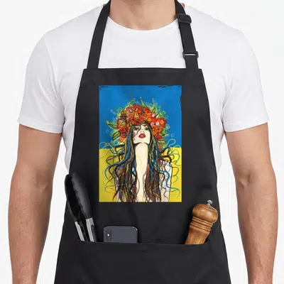 Village ukrainian aprons - Cartoon woman with red flower crown and flowing hair on blue and yellow background — shown on a black cotton canvas apron against a white background