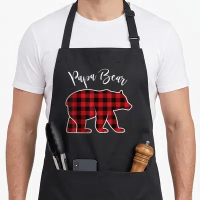 Pajama buffalo apron - Papa Bear text above red and black plaid bear silhouette in cartoon style — shown on a black cotton canvas apron against a white background