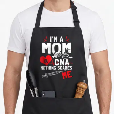 Scare white nurse apron - Stacked I'm a Mom CNA text with red heart EKG line stethoscope and syringe graphics — shown on a black cotton canvas apron against a white background