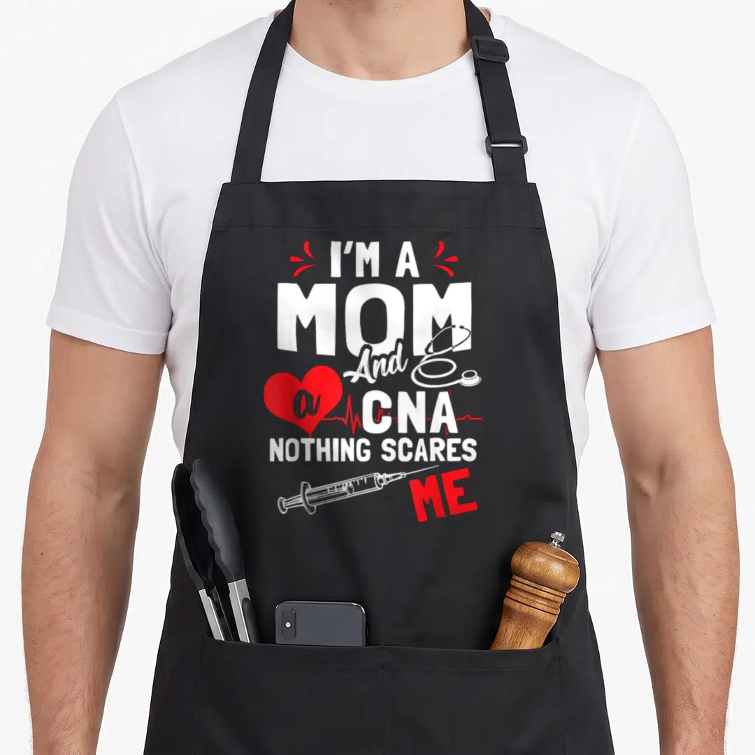 Scare white nurse apron - Stacked I'm a Mom CNA text with red heart EKG line stethoscope and syringe graphics — shown on a black cotton canvas apron against a white background