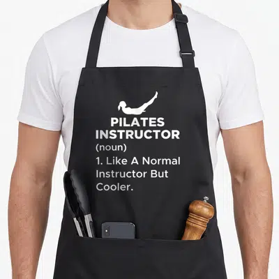 Pilate machine apron - White silhouette of pilates pose above definition text reading Like A Normal Instructor — shown on a black cotton canvas apron against a white background