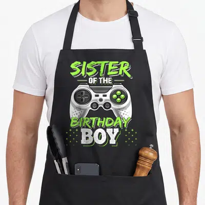 Sister video game apron - Grey game controller with lime green text Sister of the Birthday Boy — shown on a black cotton canvas apron against a white background