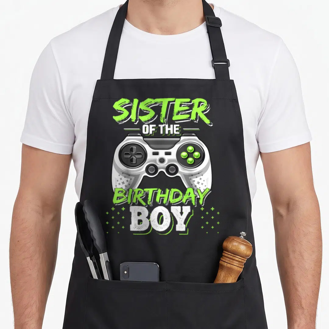 Sister video game apron - Grey game controller with lime green text Sister of the Birthday Boy — shown on a black cotton canvas apron against a white background