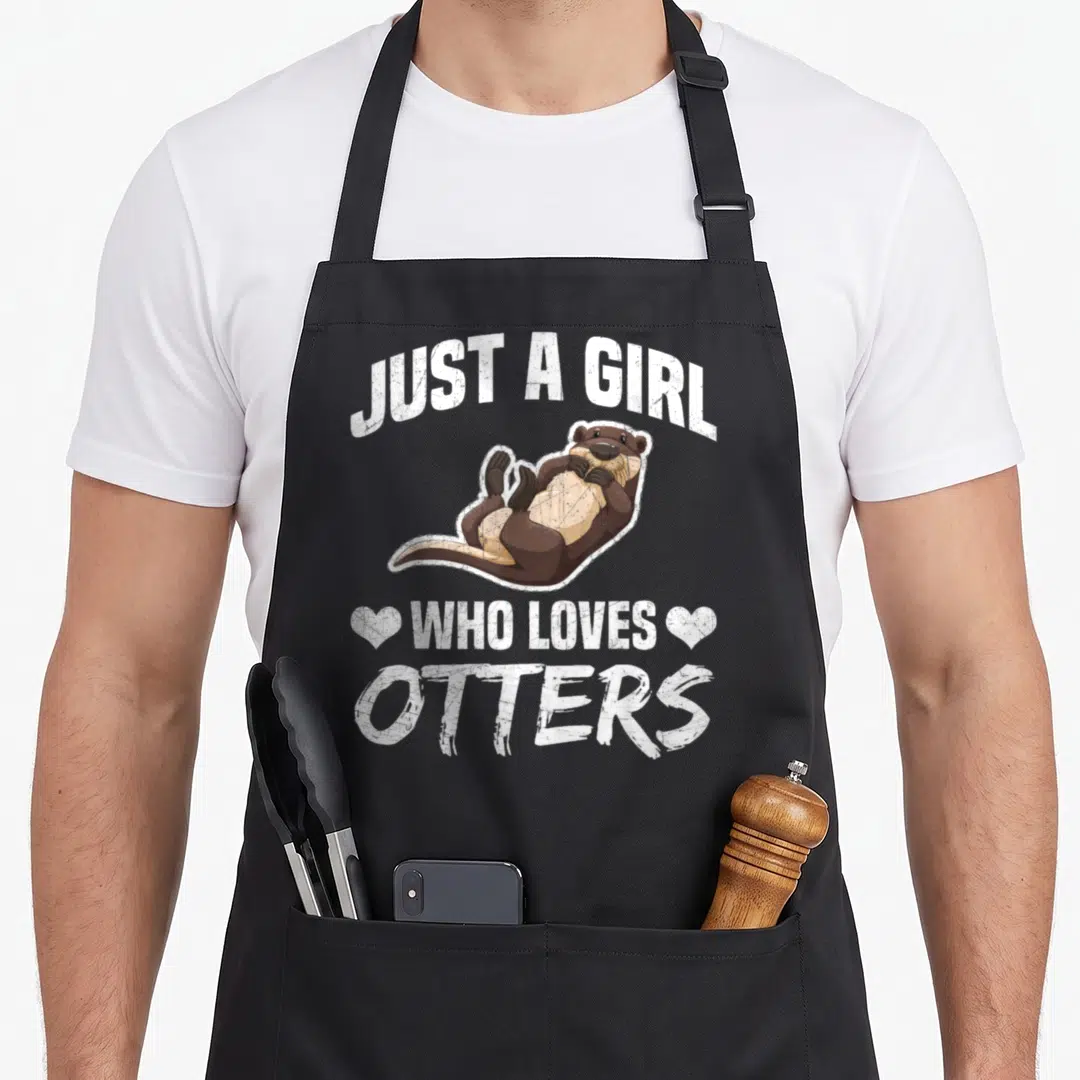 Retro otter apron - Cartoon otter floating between JUST A GIRL WHO LOVES OTTERS text and two hearts — shown on a black cotton canvas apron against a white background