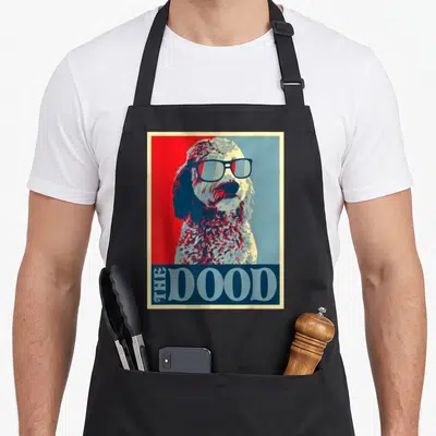 Doodle goldendoodle apron - Retro dog wearing sunglasses with THE DOOD text on red and blue background — shown on a black cotton canvas apron against a white background