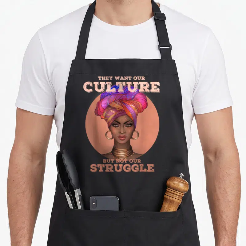 Culture african american aprons - Woman in colorful headwrap inside peach circle with text They Want Our Culture — shown on a black cotton canvas apron against a white background