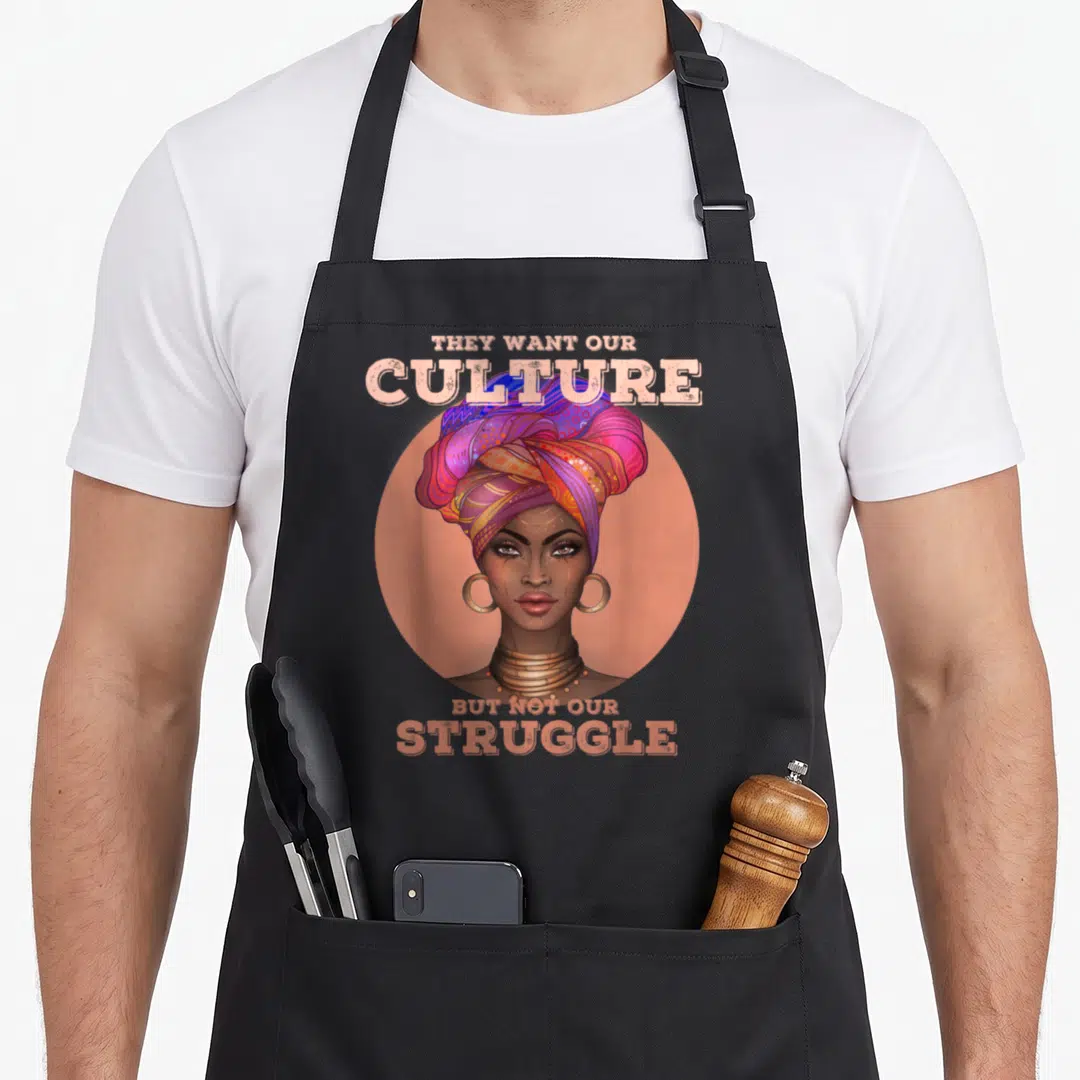 Culture african american aprons - Woman in colorful headwrap inside peach circle with text They Want Our Culture — shown on a black cotton canvas apron against a white background