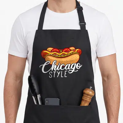 Chicago hotdog hot dog apron - Cartoon hot dog with mustard tomato relish and Chicago STYLE text below — shown on a black cotton canvas apron against a white background
