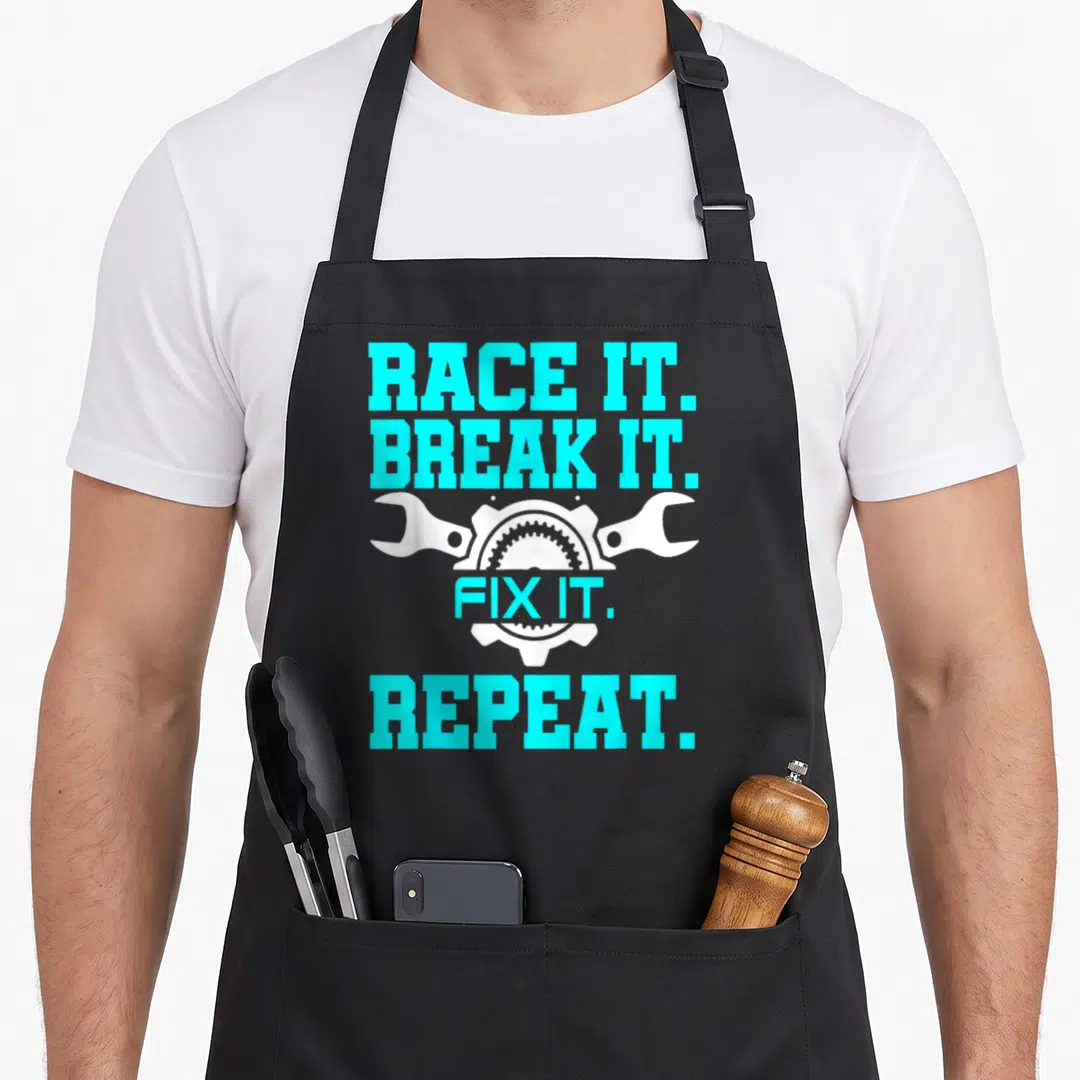 Racing auto mechanic apron - Cyan text RACE IT BREAK IT FIX IT REPEAT over white gear and two wrenches — shown on a black cotton canvas apron against a white background