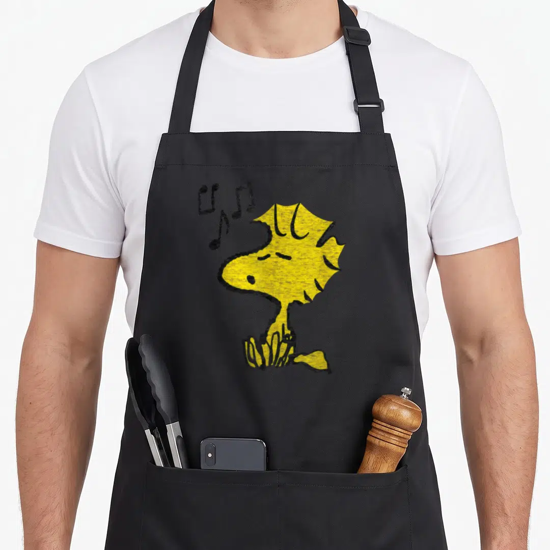 Woodstock singing apron - Yellow bird line art with black musical notes and grass details — shown on a black cotton canvas apron against a white background
