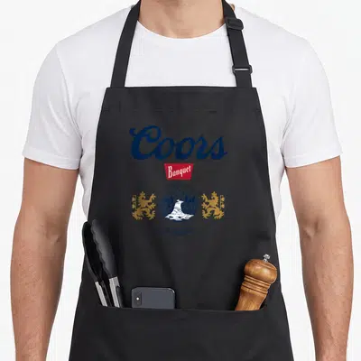 Coor colorado apron - Vintage Coors Banquet logo with gold lions, mountain emblem, and brewery text in blue red and gold — shown on a black cotton canvas apron against a white background
