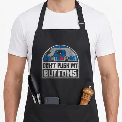 Droid x apron - Distressed R2-D2 head in arch above DON'T PUSH MY BUTTONS text blocks — shown on a black cotton canvas apron against a white background