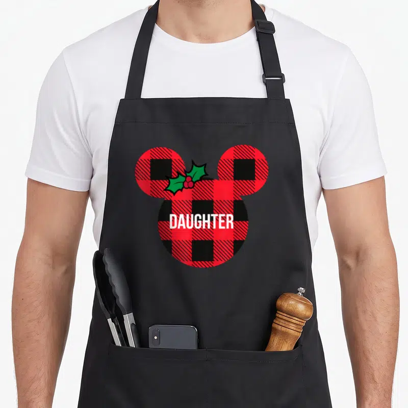 Daughter holiday plaid apron - Mouse head silhouette in red black plaid with white DAUGHTER text and green holly — shown on a black cotton canvas apron against a white background