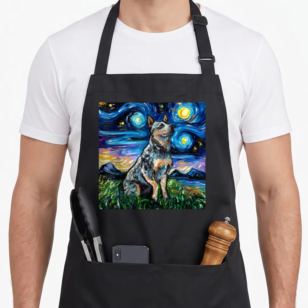 Blue dog apron - Realistic heeler dog sitting on green grass under a swirling blue starry night sky — shown on a black cotton canvas apron against a white background
