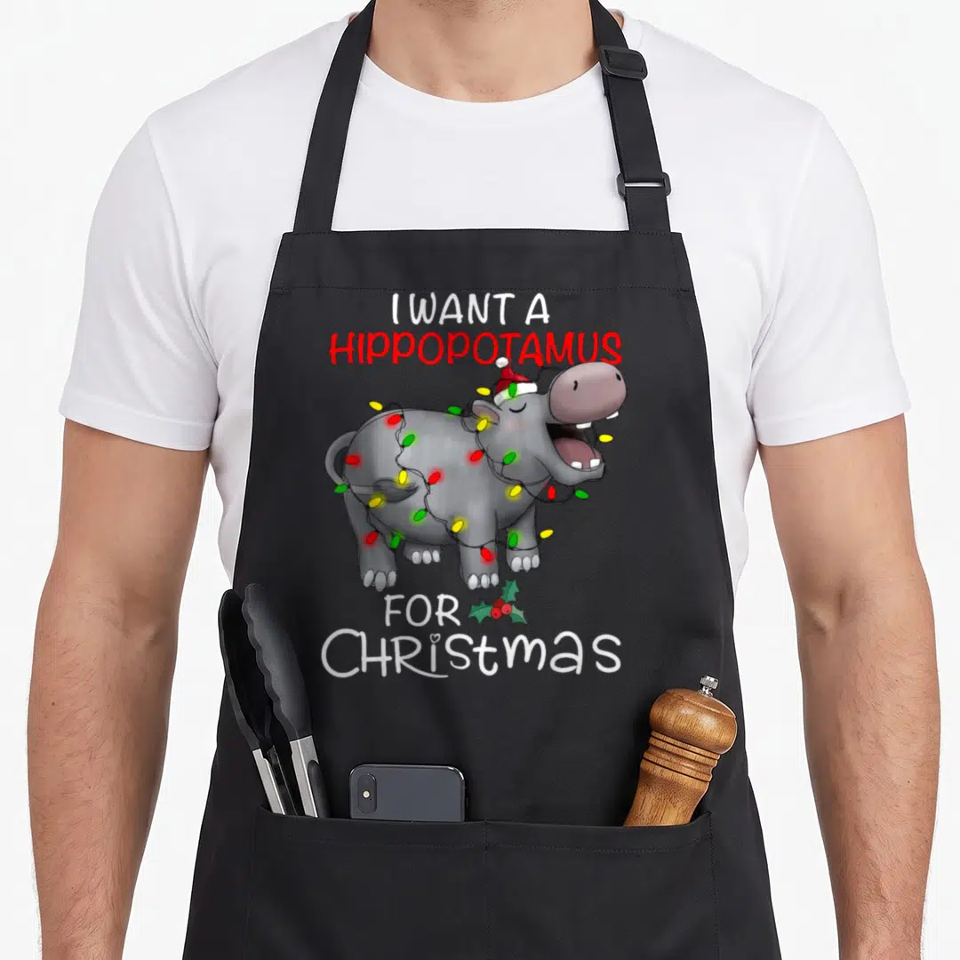 Hippopotamus xmas hippo christmas apron - Cartoon grey hippo wearing Santa hat and string lights with I want — shown on a black cotton canvas apron against a white background