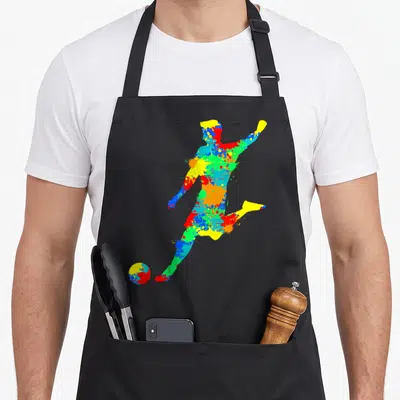 Player boy soccer apron - Soccer player silhouette filled with blue red yellow and green paint splatters kicking a ball — shown on a black cotton canvas apron against a white background