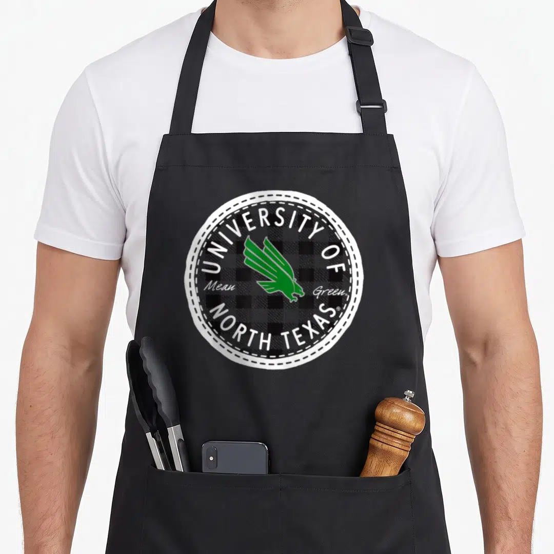 North university of texas apron - Green eagle inside black and white plaid circle with arched university text — shown on a black cotton canvas apron against a white background