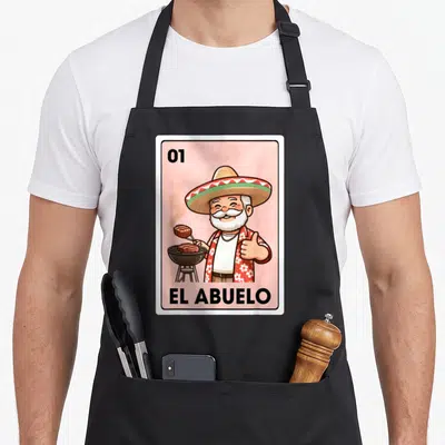 Grandpa mexican apron - Cartoon grandfather grilling steak on pink background with text 01 EL ABUELO — shown on a black cotton canvas apron against a white background