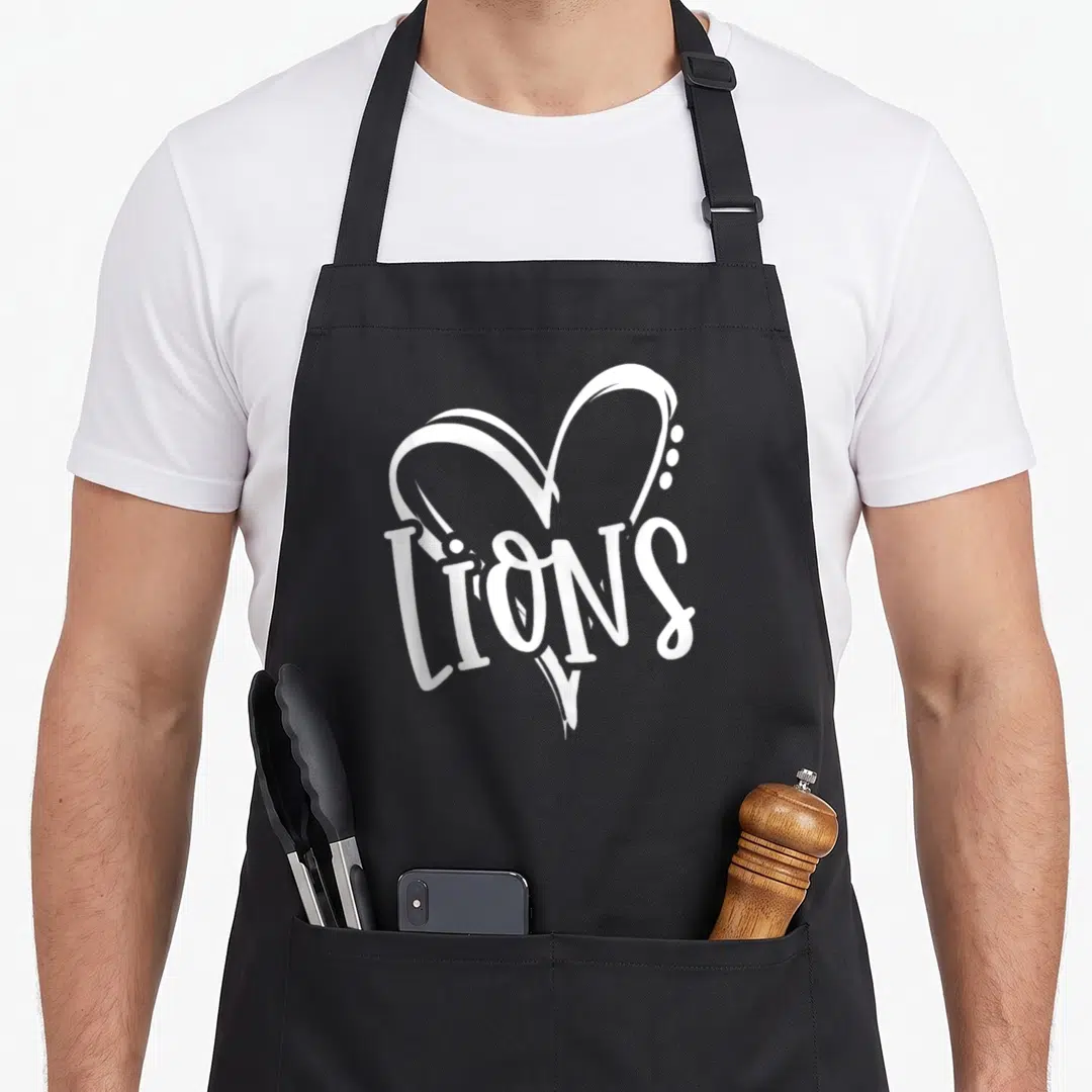 Sport lion apron - White LIONS text inside stylized heart shape on canvas fabric — shown on a black cotton canvas apron against a white background