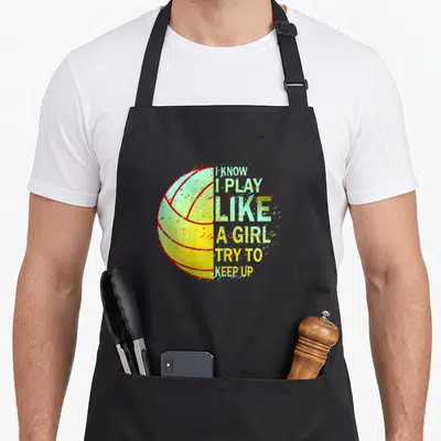 Cute girls volleyball apron - Half volleyball graphic with red outlines and stacked text I KNOW I PLAY LIKE A GIRL TRY — shown on a black cotton canvas apron against a white background