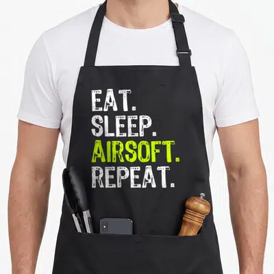 Eat airsoft apron - Stacked EAT SLEEP AIRSOFT REPEAT text in white and lime green — shown on a black cotton canvas apron against a white background