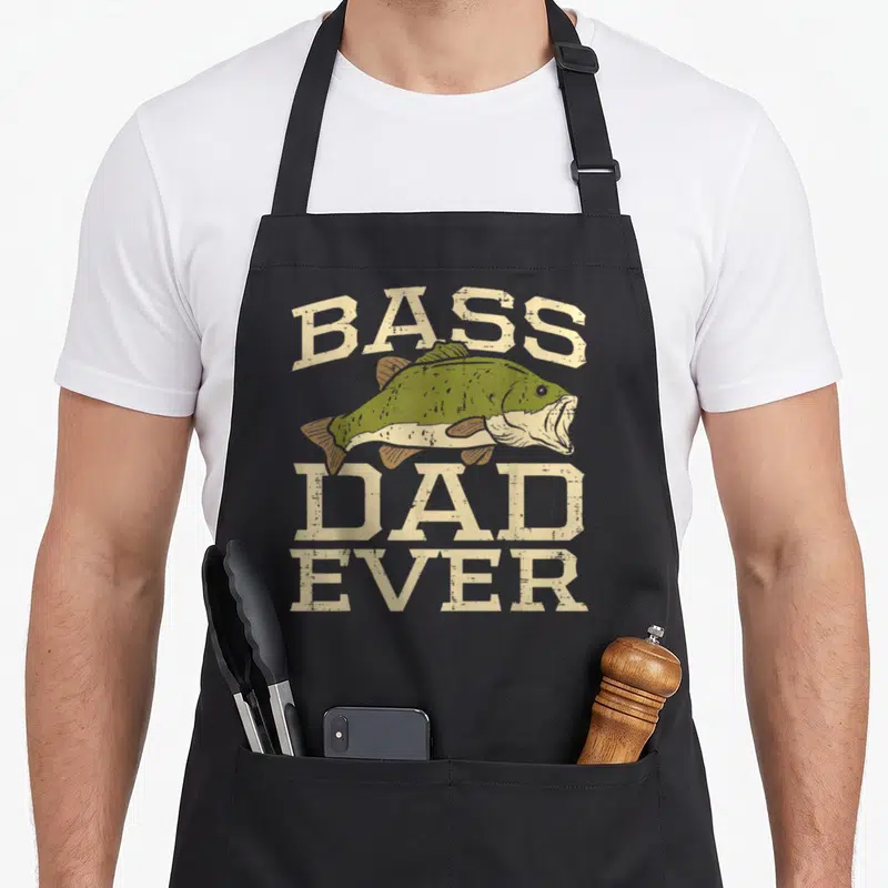 Bass father day apron - Distressed beige text reading Bass Dad Ever around an olive green bass fish illustration — shown on a black cotton canvas apron against a white background