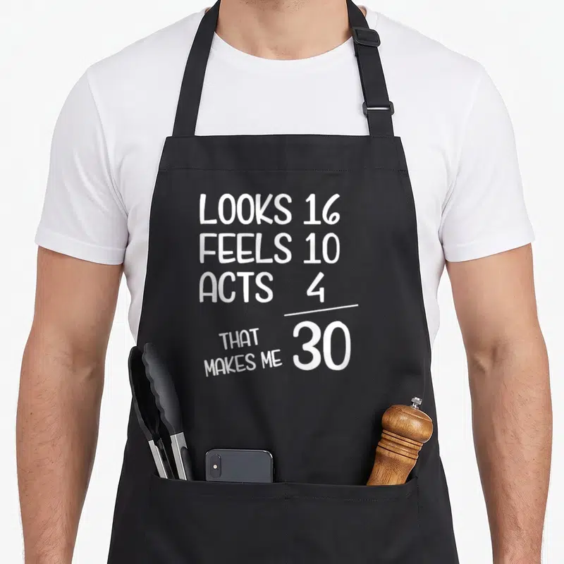 Funny 30th birthday apron - White stacked text looks 16 feels 10 acts 4 that makes me 30 — shown on a black cotton canvas apron against a white background