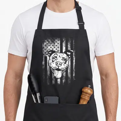 Pitbull american flag apron - White distressed dog head superimposed over a weathered American flag pattern — shown on a black cotton canvas apron against a white background