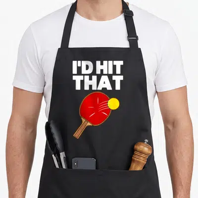 Game table apron - I'D HIT, THAT text above red paddle and yellow ball cartoon — shown on a black cotton canvas apron against a white background