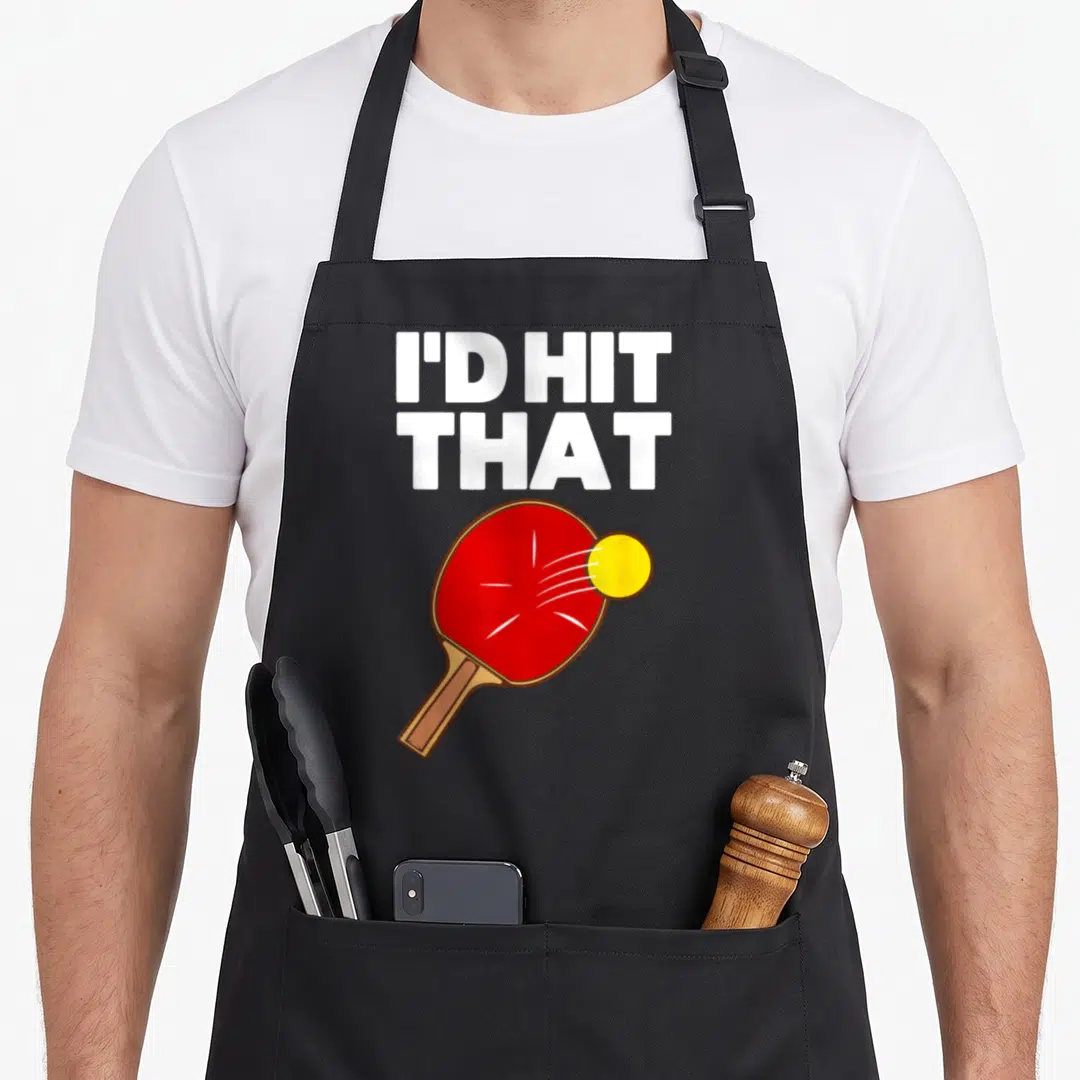 Game table apron - I'D HIT, THAT text above red paddle and yellow ball cartoon — shown on a black cotton canvas apron against a white background