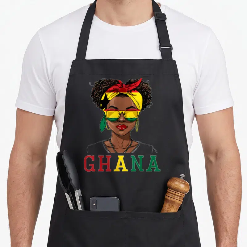 Ghana ghanaian apron - Cartoon woman in sunglasses and headwrap with GHANA text in red yellow green — shown on a black cotton canvas apron against a white background