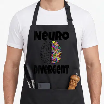 Neurodiversity brain neurodivergent apron - Brain graphic split into black and white and multicolored halves under bold — shown on a black cotton canvas apron against a white background