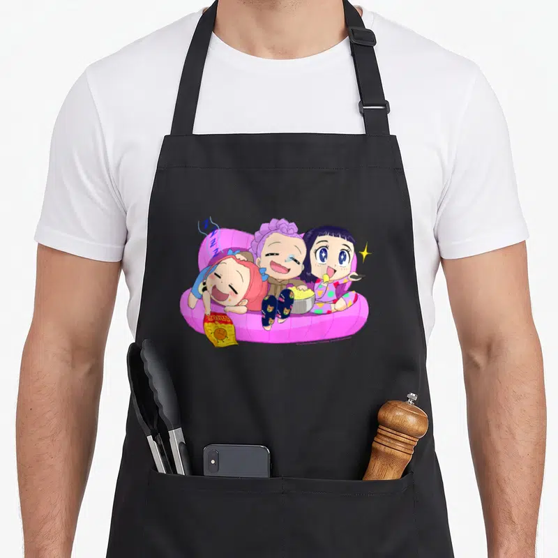Chibi halloween apron - Three cartoon girls on pink sofa with popcorn and Z Z Z text — shown on a black cotton canvas apron against a white background