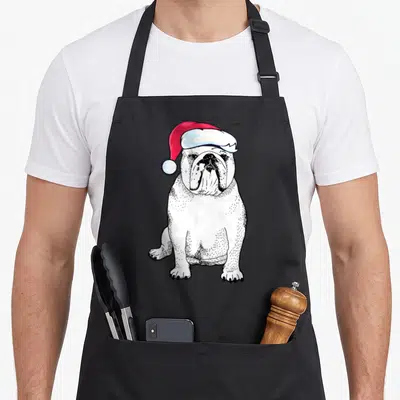 Bulldog christmas english chef aprons - Seated white bulldog wearing red Santa hat in cartoon style with black line work — shown on a black cotton canvas apron against a white background