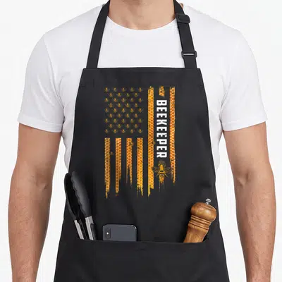 Beekeeping american flag apron - Stylized flag made of honeycomb and bees with vertical BEEKEEPER text in distressed — shown on a black cotton canvas apron against a white background