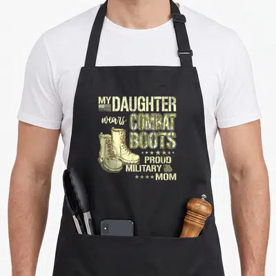 Combat mom daughter aprons - Distressed text reading My Daughter Wears Combat Boots with boots and dog tags in olive — shown on a black cotton canvas apron against a white background