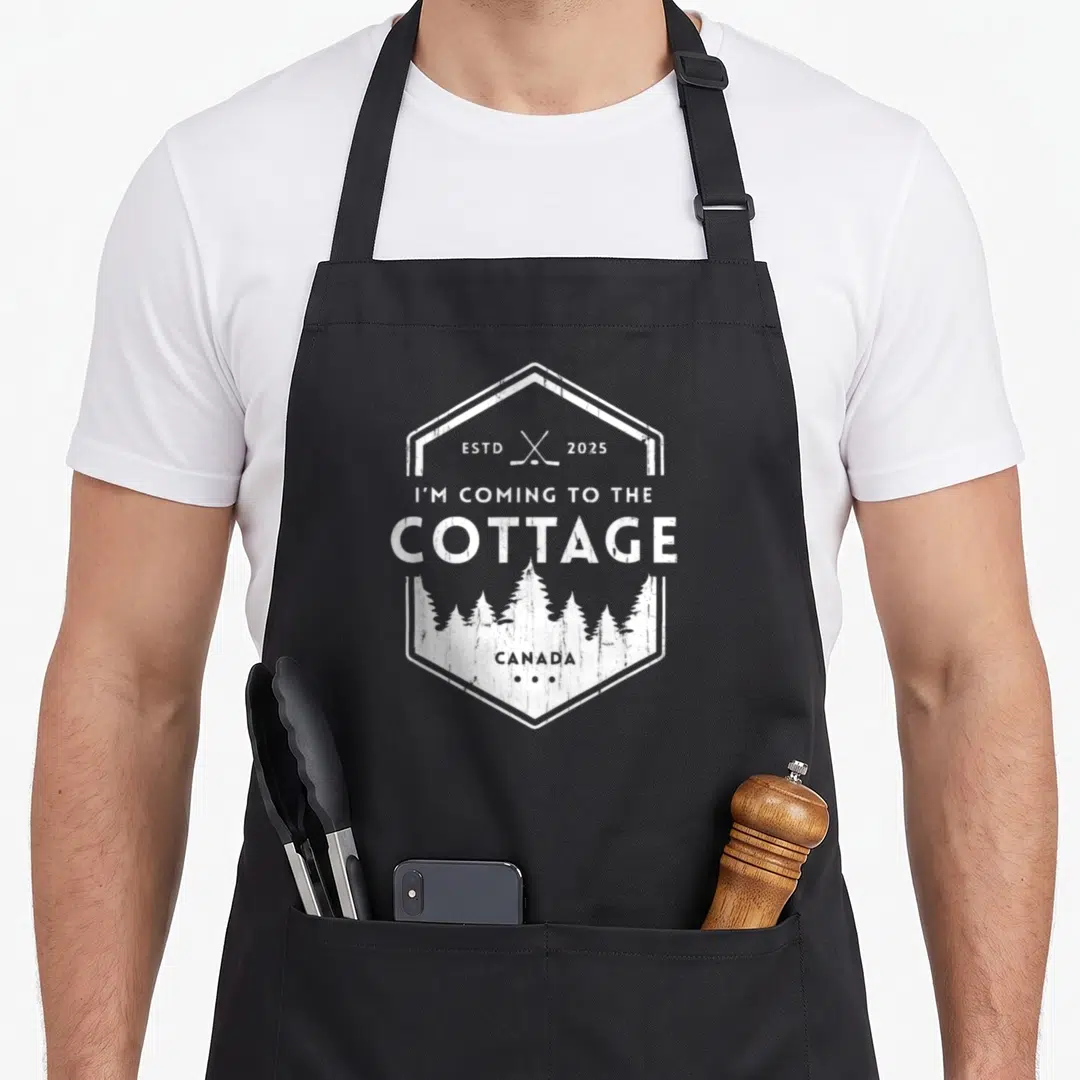 Romance cottage apron - White hexagon logo with crossed hockey sticks, pine trees, and text reading I'm Coming — shown on a black cotton canvas apron against a white background